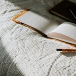 an open book sitting on top of a bed next to a pencil